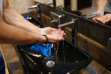 Man washes hands in the sink in bathroom at home checking temperature by touching running water with hand