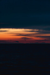 Fototapeta na wymiar Dark sunset on the sea with orange flashes of light. Vertical photo