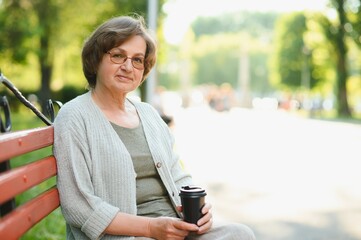 Portrait of aged positive peaceful lady sitting bench hold coffee