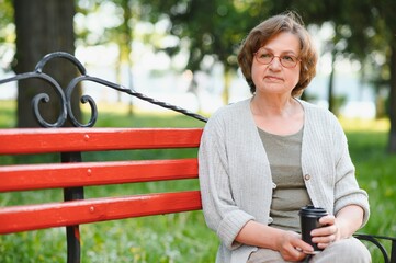 Portrait of aged positive peaceful lady sitting bench hold coffee