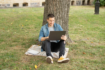 Young man with laptop rest in grass at university campus. Business man sit on lawn work outdoors on computer in a park. Student man on lesson with laptop. education and remote working concept