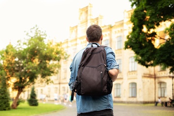 Student university standing with his back to the camera and his backpack on one shoulder and...