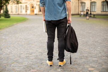 Man legs in yellow sneakers, denim shirt, black jeans at university campus. Back view of stylish...