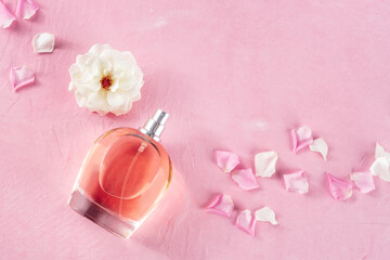 Perfume. Rose fragrance in an elegant bottle with fresh flowers and petals, overhead flat lay composition on a pink background with a place for text. Luxury perfumery product