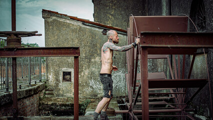 Obraz na płótnie Canvas Frustrated man with tattooed body in an abandoned site old machinery