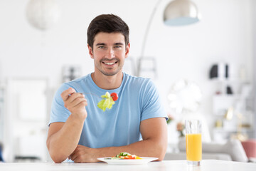 Young handsome man wears a blue t-shirt eating salad.