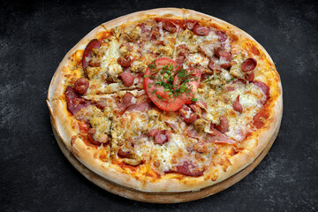 Pizza with meat sausage and chicken, cheese and tomatoes on a gray concrete background, with selective focus