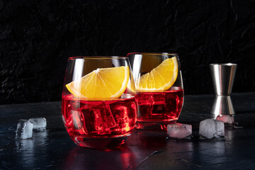 Campari aperitif with fresh orange slices and a jigger, on a black background. An alcoholic...