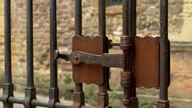Antique iron wrought rusty latch of a locked medieval lattice gate. Vintage curved retro design