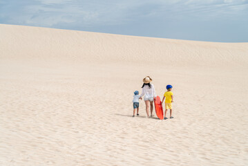 Mother with kids climbing up sand dune while carrying a sandboard, Kangaroo Island, South Australia