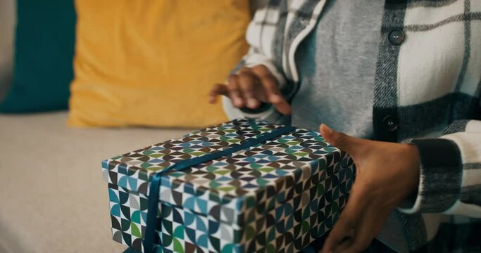 Winter evening. An African-looking girl sits on sofa and unpacks gift. Untying the blue ribbon, the girl opened the box and saw not what she wanted. The girl was disappointed and set the box aside.