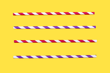 Four multi-colored striped drinking straws are arranged parallel in a row on a yellow background. Paper eco-friendly drinking accessories in the form of striped straws