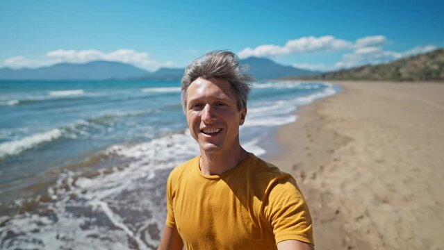 close up selfie portrait of happy middle aged greyhead man at sea coast enjoys sunny day on beautiful sandy beach Iztuzu in Turkey. inspired enjoyed man makes selfie video and waves hand to camera
