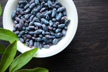 Summer honeysuckle berries with fresh leaves in white plate over wooden table