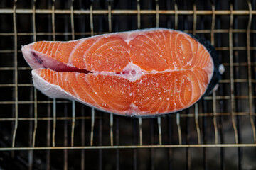 Close up of fresh salmon steak prepared for grilling with grains of salt on it, lies on grill mesh . High-quality photo