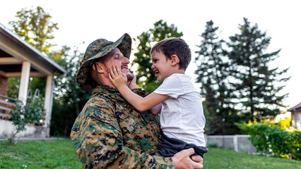 Happy reunion of young father soldier with family son outdoors. Photo of smiling man soldier and his son seeing after a long time and enjoying.