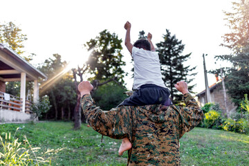 Happy male soldier dad reunited with son after army. An emotional military father, dressed in camouflage, holds his young son in arms in greeting after returning home from a tour of duty overseas.