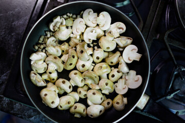 Mushrooms in the form of skulls in black frying pan. Champignons frying process. Edible Halloween Concept