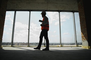 Portrait of an architect builder studying layout plan of the rooms, serious civil engineer working with documents on construction site, building and home renovation, professional foreman at work.