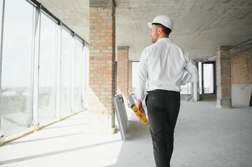 Portrait of an architect builder studying layout plan of the rooms, serious civil engineer working with documents on construction site, building and home renovation, professional foreman at work.