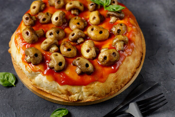 Homemade pizza with tomato sauce and mushrooms in the form of skulls. Concept for Halloween celebrations