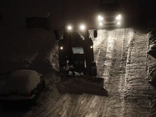 Wheeled tractor cleaning a snow with snowplow on snowy street at winter night after snowfall with...
