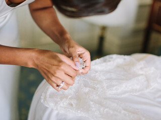 A bride with swarthy skin in a wedding ring holds a fragment of a wedding lace dress with both hands.