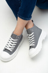 Stylish women's grey sneakers on legs of model on  white background close-up. Sports model of women's shoes for advertising, copy space.