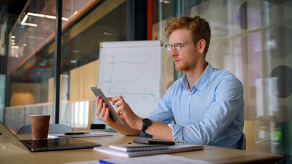 Young ethnic successful businessman holding tablet sitting in office.
