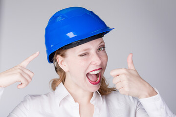 Young female engineer is pointing to her hart hat and shows thumbs-up