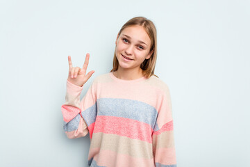 Young caucasian girl isolated on blue background showing a horns gesture as a revolution concept.