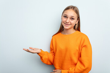 Young caucasian girl isolated on blue background showing a copy space on a palm and holding another...