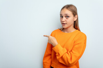 Young caucasian girl isolated on blue background smiling and pointing aside, showing something at blank space.