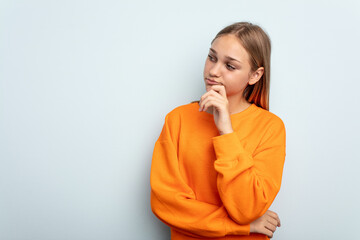 Young caucasian girl isolated on blue background relaxed thinking about something looking at a copy space.