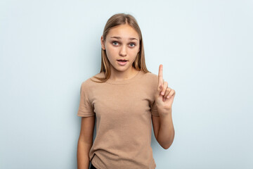 Young caucasian girl isolated on blue background pointing upside with opened mouth.