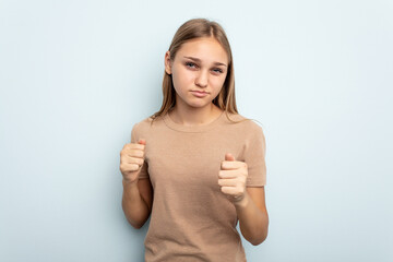 Young caucasian girl isolated on blue background showing fist to camera, aggressive facial expression.