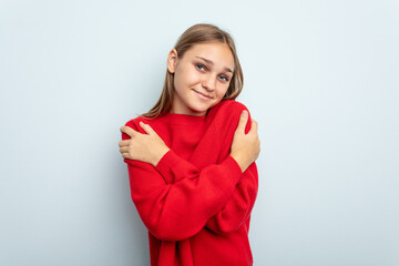 Young caucasian girl isolated on blue background hugs, smiling carefree and happy.