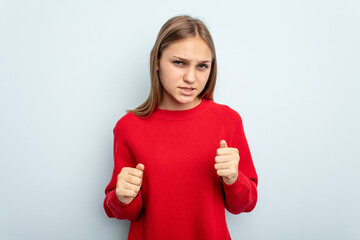 Young caucasian girl isolated on blue background upset screaming with tense hands.