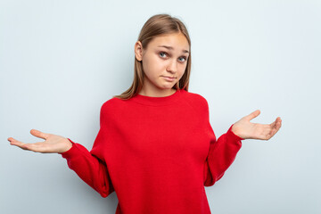 Young caucasian girl isolated on blue background doubting and shrugging shoulders in questioning...