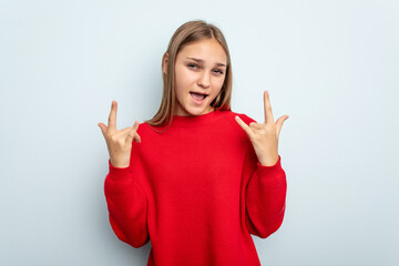 Young caucasian girl isolated on blue background showing a horns gesture as a revolution concept.