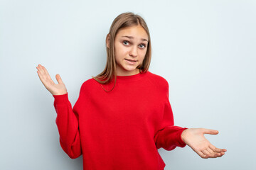Young caucasian girl isolated on blue background confused and doubtful shrugging shoulders to hold...