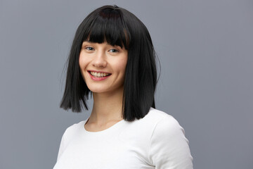 a beautiful woman is standing full-face on a dark background in a white tight T-shirt, smiling sweetly looking straight