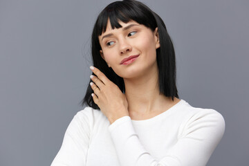 Fototapeta na wymiar a relaxed woman stands full-face against a dark background in a white tight T-shirt, straightens her hair with her hand, smiling a little, looks away in embarrassment