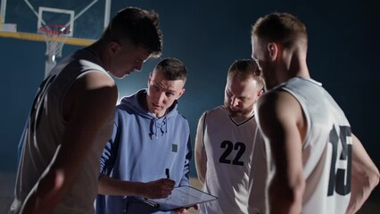 Basketball championship, the coach instructs players on the tactics of the game, using a tablet and a marker for drawing, briefing before the game. - Powered by Adobe