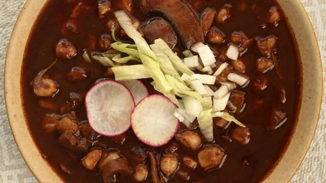 Close-up, top view of vegan Pozole Rojo with lettuce, radish and onion. Famous Mexican cuisine dish made with cacahuazintle, shredded jackfruit, mushrooms and dried chilies: guaillo, ancho, pasilla.