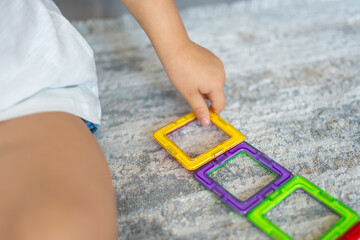 Little girl playing colorful magnet plastic blocks kit at home. The child playing educational...