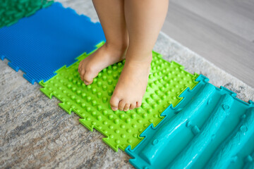 Close up view of Little girl walks on a massage mat. Toddler baby foot massage mat. Exercises for legs orthopedic massage carpet. 