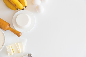 Frame of cooking cake ingredients. Flour, banana, eggs and butter on white table. Copy space. Top...