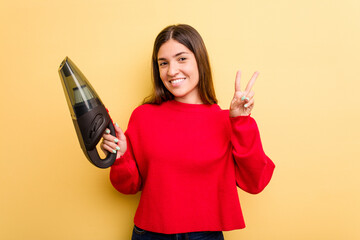 Naklejka premium Young caucasian woman holding a hand vacuum cleaner isolated on yellow background showing number two with fingers.