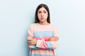 Young caucasian woman isolated on blue background blows cheeks, has tired expression. Facial expression concept.